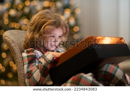Child in Santa red hat holding Christmas gift. Christmas and New Year concept. Surprise kid opening Christmas present gift box.