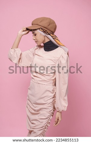 Close up portrait of a beautiful Asian female model wearing dress and hijab with hat isolated over pink background. Stylish Muslim female fashion lifestyle concept.