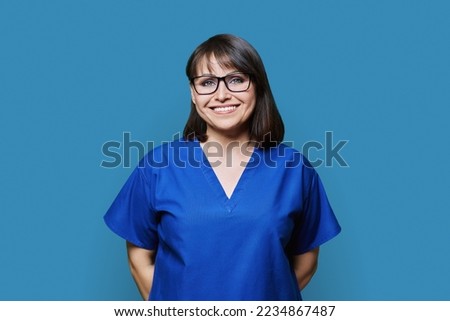 Smiling woman in blue scrubs uniform looking at camera on blue background Royalty-Free Stock Photo #2234867487