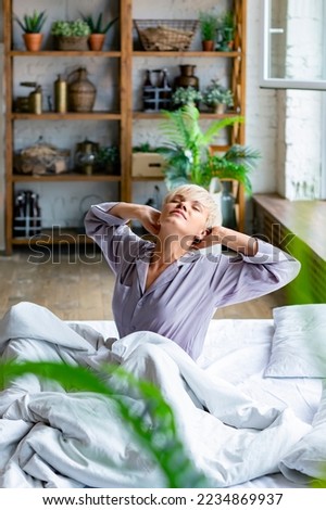 Vertical photo of a young blonde woman woke up and stretching. She stretched her arms and enjoys the day off. Format photo 2x3.