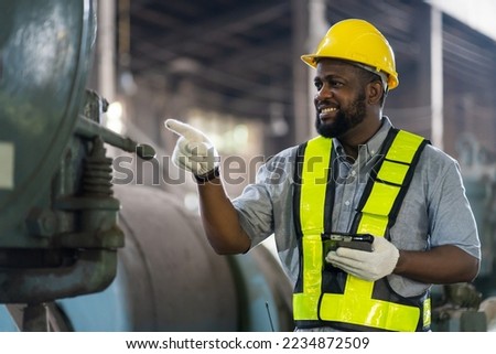African American male worker checking or maintaining machine at the industry factory area. Male worker wear safety helmet and uniform working in the factory Royalty-Free Stock Photo #2234872509