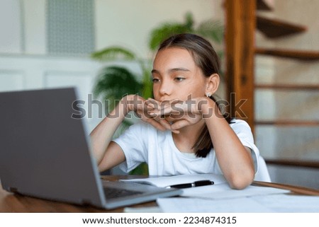 Close up photo of a teenage girl in front of a laptop. She's listening to a boring online lesson or doing her homework. Concept of online learning and modern technologies in education.