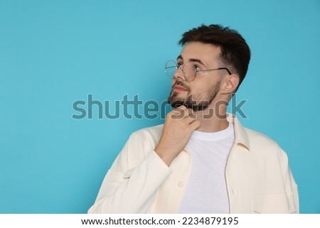 Thoughtful man in white jacket and eyeglasses on light blue background, space for text