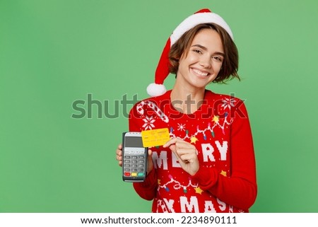 Merry young woman wear xmas sweater Santa hat posing hold wireless bank payment terminal process acquire credit card isolated on plain pastel light green background Happy New Year 2023 holiday concept