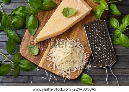 Parmesan cheese with grater on a cutting board. Whole wedge and grated grana padano cheese, stainless steel grater and fresh basil herb on a wooden background. Dairy product. Top view. Royalty-Free Stock Photo #2234893045