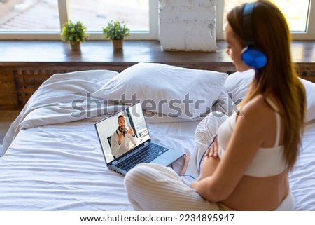 Photo of a pregnant woman sits at home on a bed in front of a laptop monitor - online consultation with a doctor.