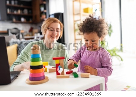 Mother looking at a child playing with an educational didactic toy. Young woman and child playing with didactic toys Royalty-Free Stock Photo #2234901369