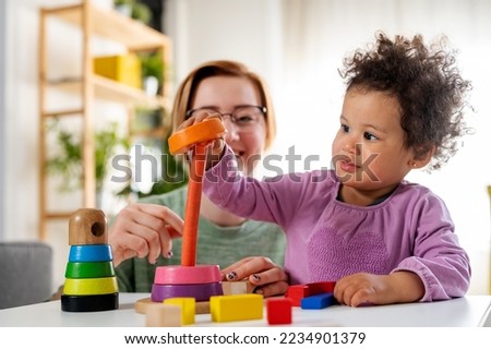 Mother looking at a child playing with an educational didactic toy. Young woman and child playing with didactic toys Royalty-Free Stock Photo #2234901379