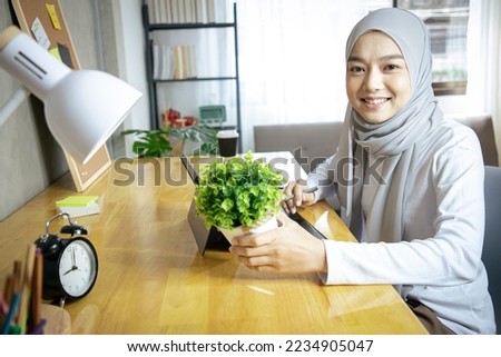 Charming Asian muslim woman in headscarf casual wear using laptop in living room at house. Remotely working from home, social distancing, quarantine for corona virus prevention. Education and working