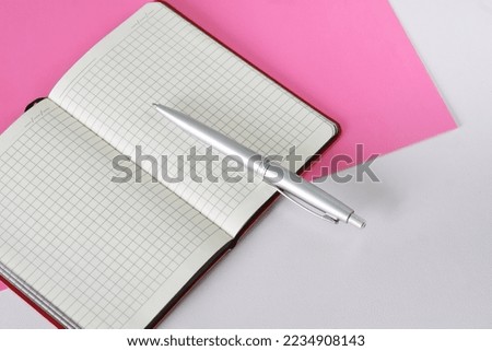 An open checkered notepad or diary and a silver fountain pen lie on a dark two-tone white and pink surface. Copy space. Close-up