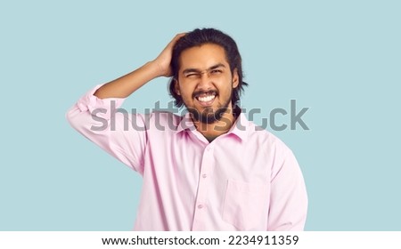 Portrait of funny man who forgot something or made mistake and scratches his head in confusion. Embarrassed young Indian man in pink shirt on pastel light blue background. Web banner. Royalty-Free Stock Photo #2234911359