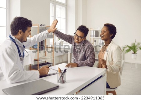 Excited male doctor and ethnic couple give high five celebrate good health results. Smiling surgeon or GP congratulate happy multiethnic family with amazing news. Recovery and medical treatment. Royalty-Free Stock Photo #2234911365