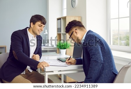 Concluding contract. Man signs lease or purchase agreement given to him by bank manager or real estate agent. Smiling male realtor or financial advisor in office watching client sign contract. Royalty-Free Stock Photo #2234911389