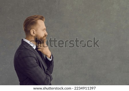 Side view portrait handsome bearded man in jacket looking hand on chin at text copyspace on grey background. Experienced business finance professional thinking about interesting quote or project idea
