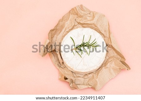 Delicious fresh italian Camembert cheese. Fresh Camembert cheese with rosemary on a food paper on pink background. Top cheese of Italy - Camembert. Italian camembert cheese top view.