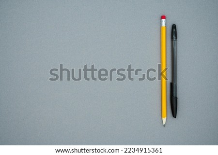 A long yellow pencil and black pen, on a gray background, copy space for text. Top view. Flat lay style. School office supplies.
