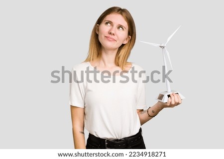 Young caucasian woman holding a small wind energy mill isolated dreaming of achieving goals and purposes