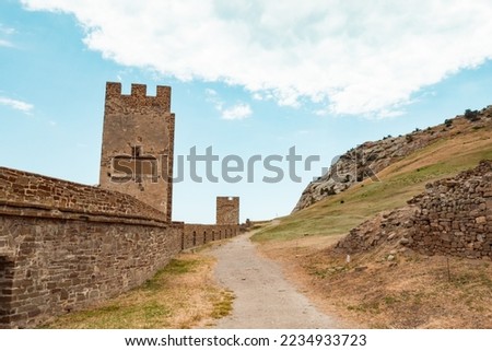 An old medieval wall and a mountain in the background. A large wall with a tower against a light blue sky.