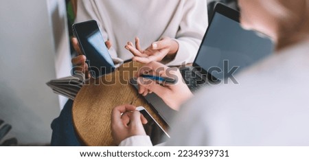 Cropped image of female colleagues discussing browsed web publication on modern cellphone technology using 4g wireless connection in coworking space for collaborative meeting, content in social media