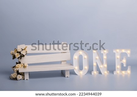 Celebratory background design for birthday a white bench with white flowers stands on a blue background. One year birthday party decorations. festive glowing letters one. 