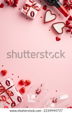 Valentine's Day concept. Top view vertical photo of gift boxes wine bottle heart shaped candles chocolate candies and two glasses with confetti on isolated light pink background with empty space