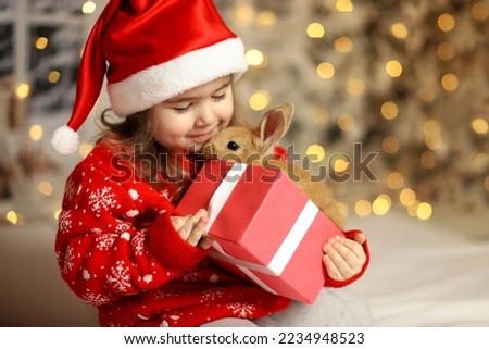  Christmas card with a baby and a rabbit in a box. Child is happy with a New Year's gift. The background is defocused light. Concept of Christmas and New Year. High quality photo
