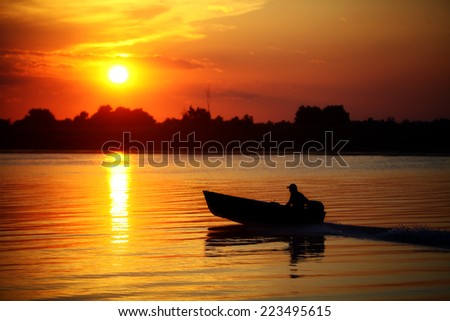 Color picture of people in a boat on a river at sunset.