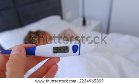 Close-up thermometer. Mother measuring temperature of her ill kid. Sick child with high fever laying in bed and mother holding thermometer. Royalty-Free Stock Photo #2234965809