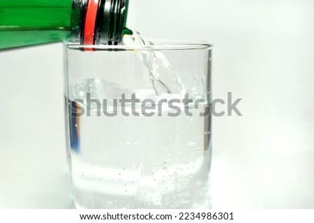 Pouring bottled mineral water for drinking into a glass, on a white background