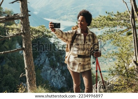 Mature black woman making a selfie while standing on the top a hill and enjoying the view during her hike in the mountains. Royalty-Free Stock Photo #2234996897