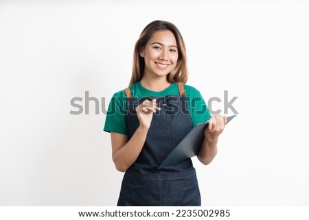 Charming young Asian businesswoman owner wearing an apron holding With clipboard front of an isolated over white background.