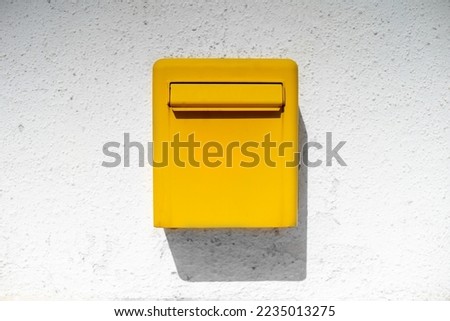 Yellow bright metal mailbox hangs on white rough wall casting shadow from sun. Stylish detail in interior of house authentic street box for letters postcards. Background good news holiday messages Royalty-Free Stock Photo #2235013275