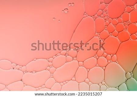 Art effect of circular bubble encircled  by many smaller bubbles created by adding oil droplets to the surface of water with the addition of liquid soap and orange -green colour  lighting.
