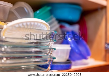 Narrow depth of field picture of an open kitchen cabinet with an assortment of containers and mismatched lids stacked.