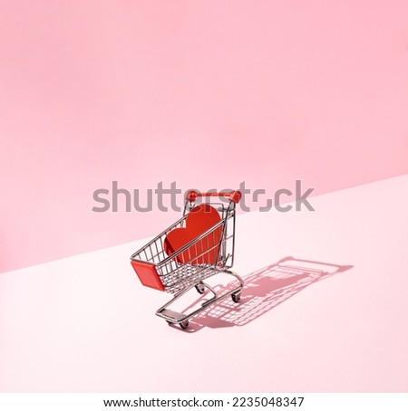 Red heart in shopping cart on pink background. Creative love or Valentines minimal concept.