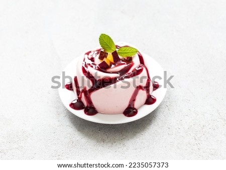 Plum cream jelly pudding with sauce, in the shape of a rose, on a plate. Light grey background	
