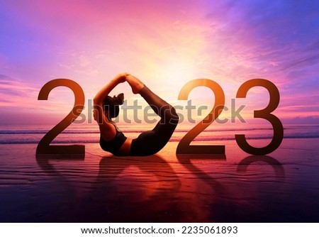 Happy new year card 2023. Silhouette of healthy girl doing Yoga One Legged Pigeon pose on tropical beach with sunset sky background, woman practicing yoga as a part of the Number 2023 sign.