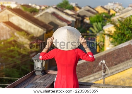happy woman wearing Ao Dai Vietnamese dress, traveler sightseeing view at rooftop in Hoi An ancient town. landmark and popular for tourist attractions. Vietnam and Southeast travel concept Royalty-Free Stock Photo #2235063859