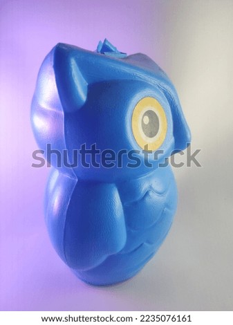 blue piggy bank, in the shape of an owl, made of plastic, which is inserted through the head