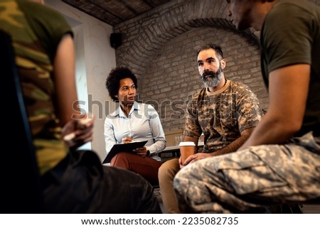 Female psychologist talking to group of diverse veterans during PTSD support group. Royalty-Free Stock Photo #2235082735