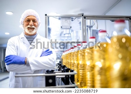 Portrait of food industry expert or technologist in white sterile uniform and standing by conveyor belt machine holding his arms crossed. Royalty-Free Stock Photo #2235088719