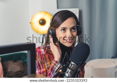 Latin american young woman smiling wearing headphones standing in living room recording song using professional setup. Horizontal indoor shot . High quality photo