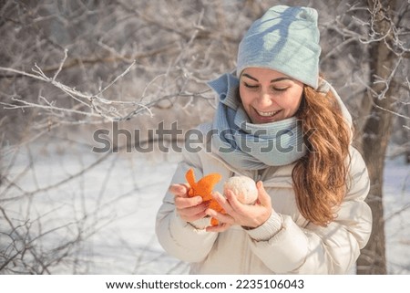 Portrait cute funny winter woman in warm clothes eat fresh orange mandarin outdoor forest park with positive emotion. Cheerful playful female relaxing smiling enjoy freedom walking frozen wood garden Royalty-Free Stock Photo #2235106043