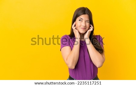 Teenager Brazilian girl over isolated yellow background frustrated and covering ears Royalty-Free Stock Photo #2235117251