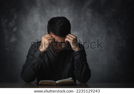 Asian man reading book or bible hand over head having stressful depression sad time sitting on the table. Depression man sad serios reading book. Education learning bible religion concept. Royalty-Free Stock Photo #2235129243