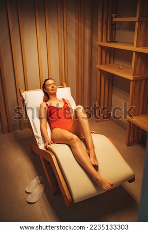 Young woman relaxing in a sauna. Interior of new Finnish sauna, infrared panels for medical procedures, classic wooden sauna. Serene woman relaxing in infrared sauna. Spa treatment