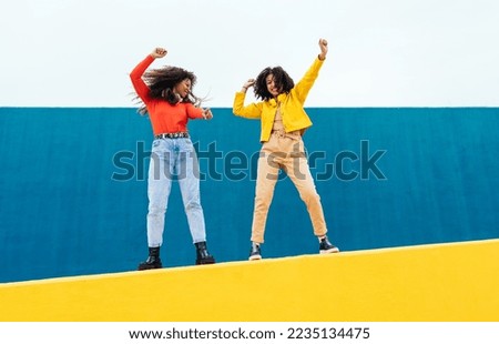 Young happy women dancing and having fun outdoor. Teenagers listening to music with smartphone and headphones in a yellow and blue modern urban area