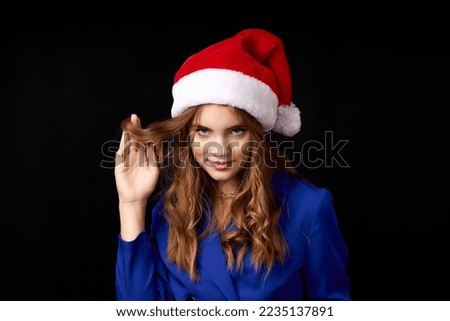 caucasian girl with long hair in blue dress wearing santa claus hat isolated on black background. High quality photo