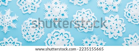 Different white snowflake shapes created from paper on light blue table background. Pastel color. Closeup. Top view. Handmade decoration elements for winter festive. Wide banner.