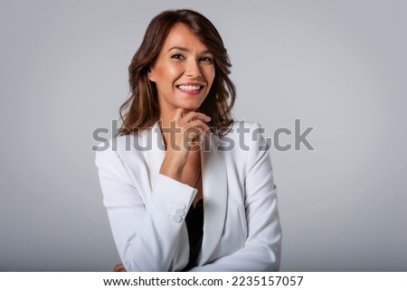 Close-up of an attractive middle aged woman with toothy smile wearing blazer while standing at isolated dark background. Copy space. Studio shot. Royalty-Free Stock Photo #2235157057